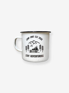 Pictured is a white enamel mug with a simple handle. In black on the front of the mug is written Camp SMRT EST 2020 on top and Stay Adventurous on the bottom. In between is a drawing - still in black - of 3 overlapping mountains over 4 simple pine trees and a Land Rover Defender 110 SUV with a SMRT Tent hard shell roof top tent on the roof rack. Great to enjoy in your roof top tent! Available for sale by SMRT Tent in Denver, Colorado, USA.